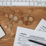 Top view of tax forms, coins on a wooden desk with a keyboard.